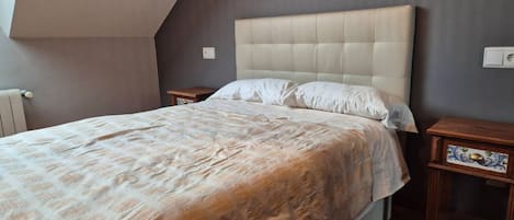 A bedroom with a large bed, a headboard, two nightstands, and artwork on the wall.