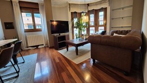 Uma sala de estar com sofá, televisão, piso de madeira e janela com cortinas.