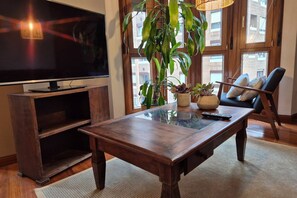 A living room with a TV, wooden coffee table, and a large plant. - 1A137 Apartamento con encanto puerto deportivo (Gijón)