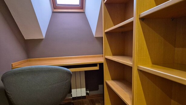 Um quarto com teto inclinado, uma escrivaninha, uma cadeira e estantes embutidas.