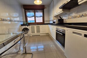 A compact kitchen with a washing machine, oven, and a glass dining table. - 1A137 Apartamento con encanto puerto deportivo (Gijón)