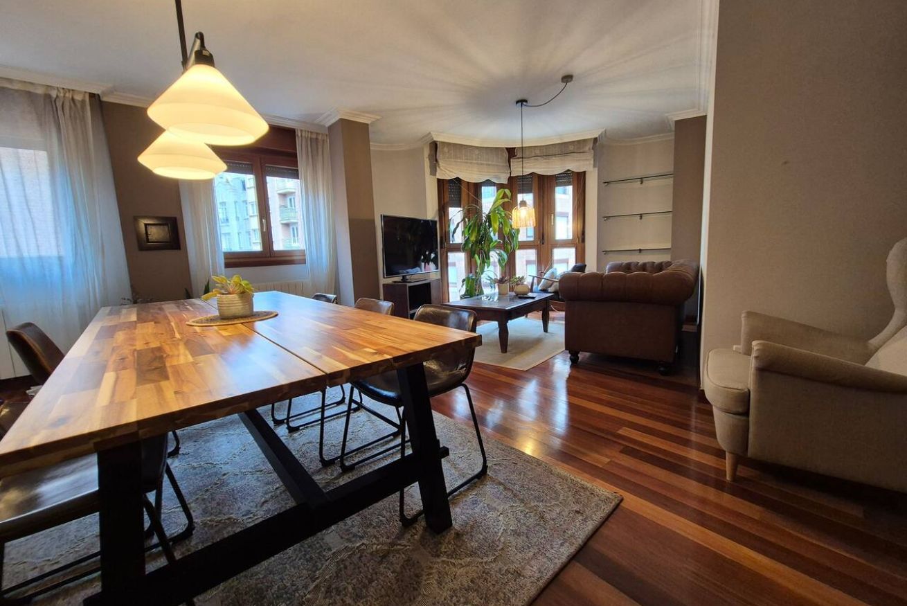 A dining area with a wooden table and chairs, a sofa, and a television.
