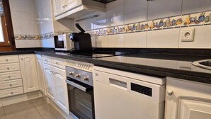 Uma cozinha com armários brancos, bancada preta, micro-ondas, torradeira, forno e lava-louças.
