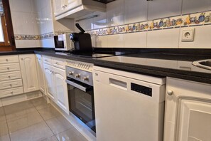 Una cucina con mobili bianchi, un piano di lavoro nero, un forno a microonde, un tostapane, un forno e una lavastoviglie.