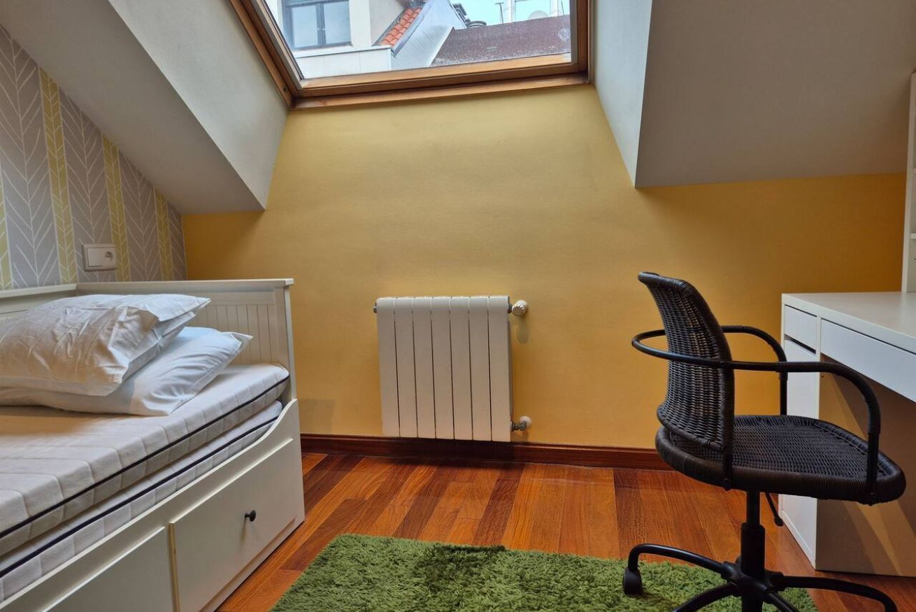 A bedroom with a bed, a radiator, a window, a desk, and a chair.