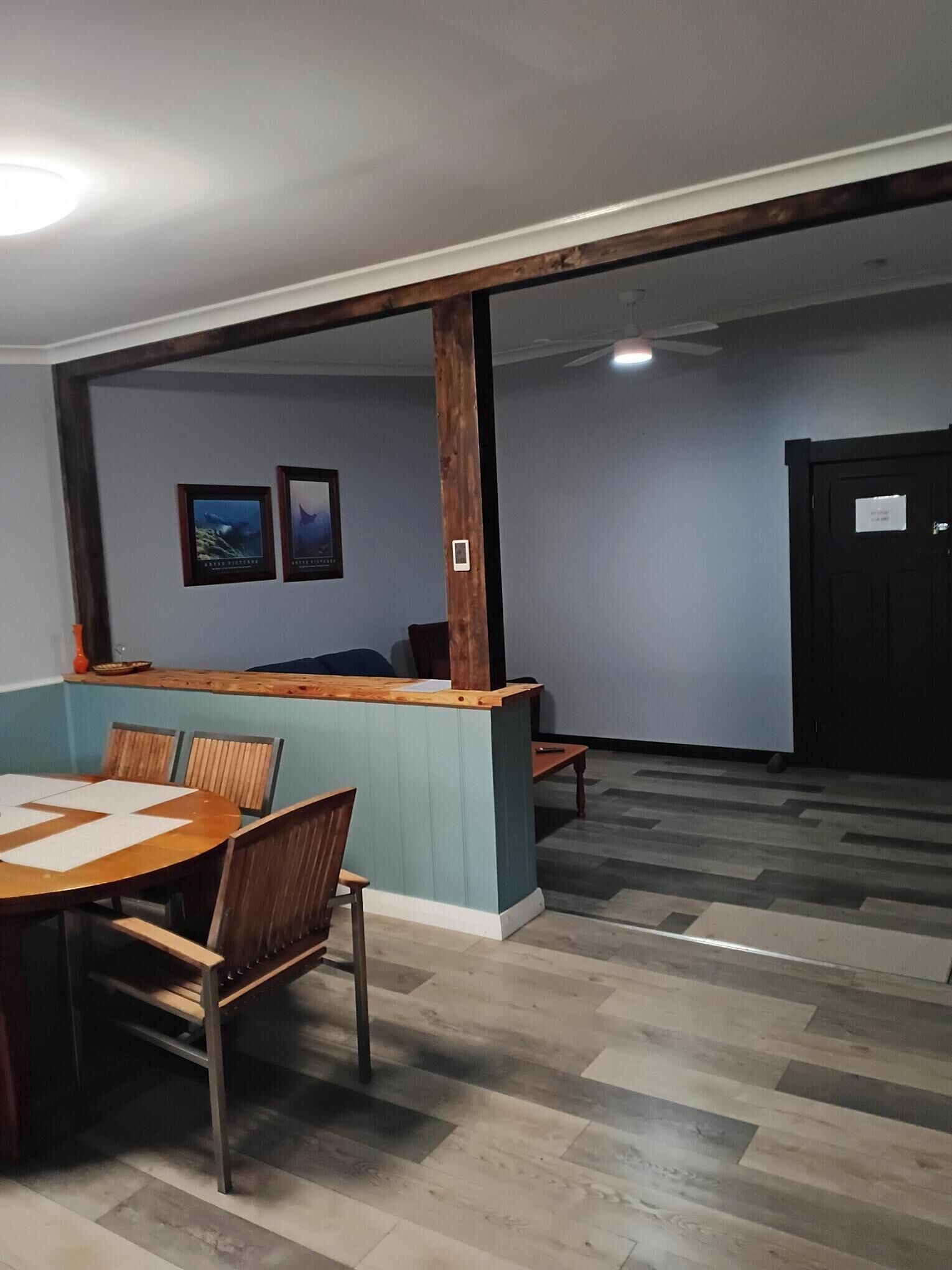 Une pièce avec un comptoir d’accueil en bois, une table ronde entourée de chaises et un ventilateur de plafond.