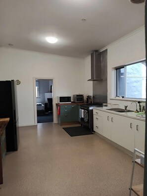 A kitchen with white cabinets, a stove, microwave, and a sink. - Port Neill SA Stone Cottage Close to everything in Pt Neill Sleeps 6 (Port Neill)