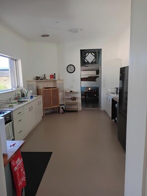 Eine Küche mit weißen Schränken, einem schwarzen Kühlschrank, einer Uhr und einem Fenster.