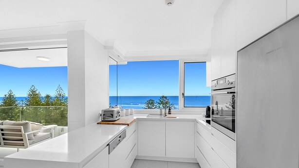 Eine moderne Küche mit Meerblick, weißen Schränken und einem eingebauten Backofen.