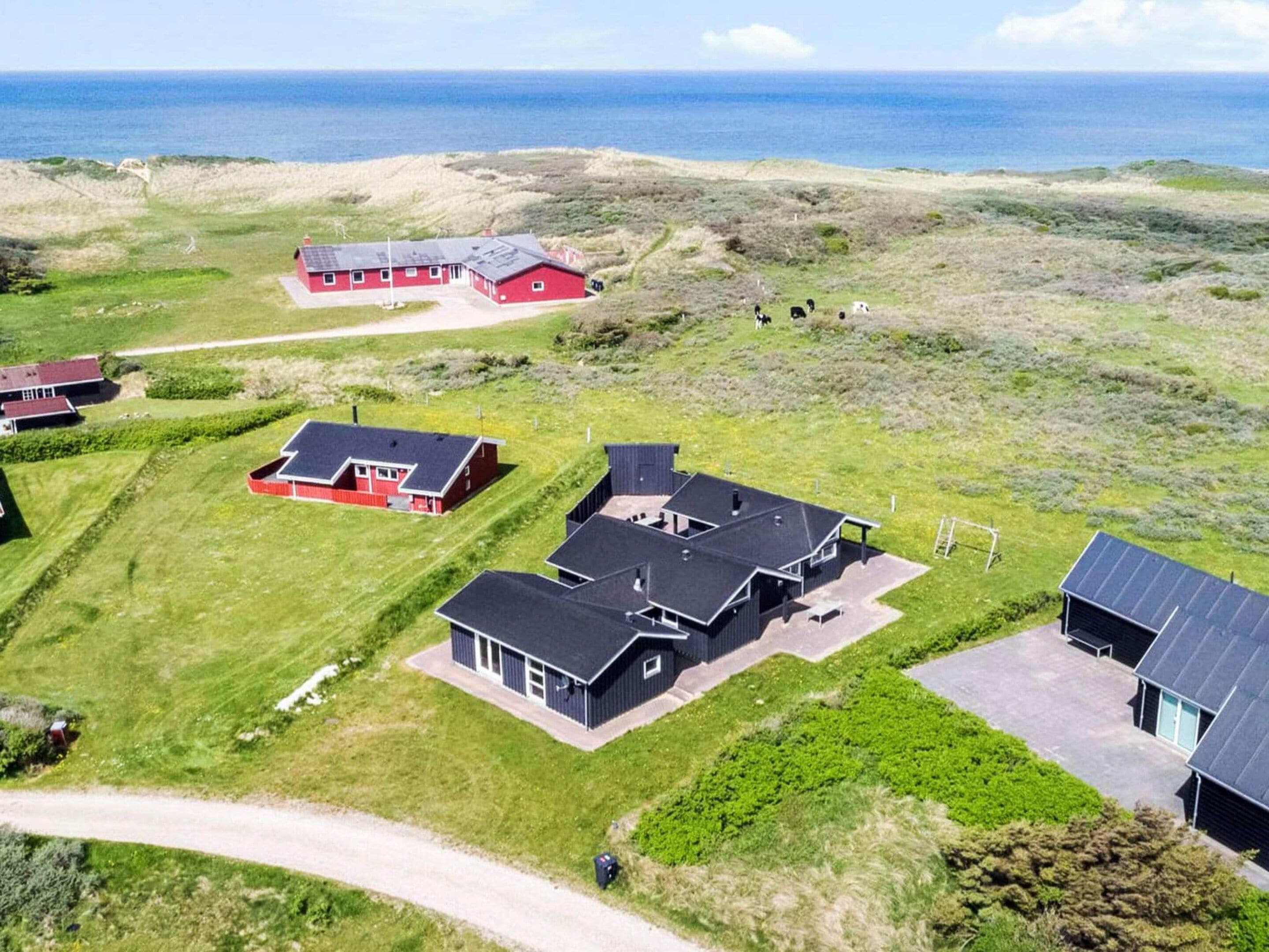 A coastal property with multiple buildings, including a main house with a large garage, a smaller red building, and a black structure with solar panels.