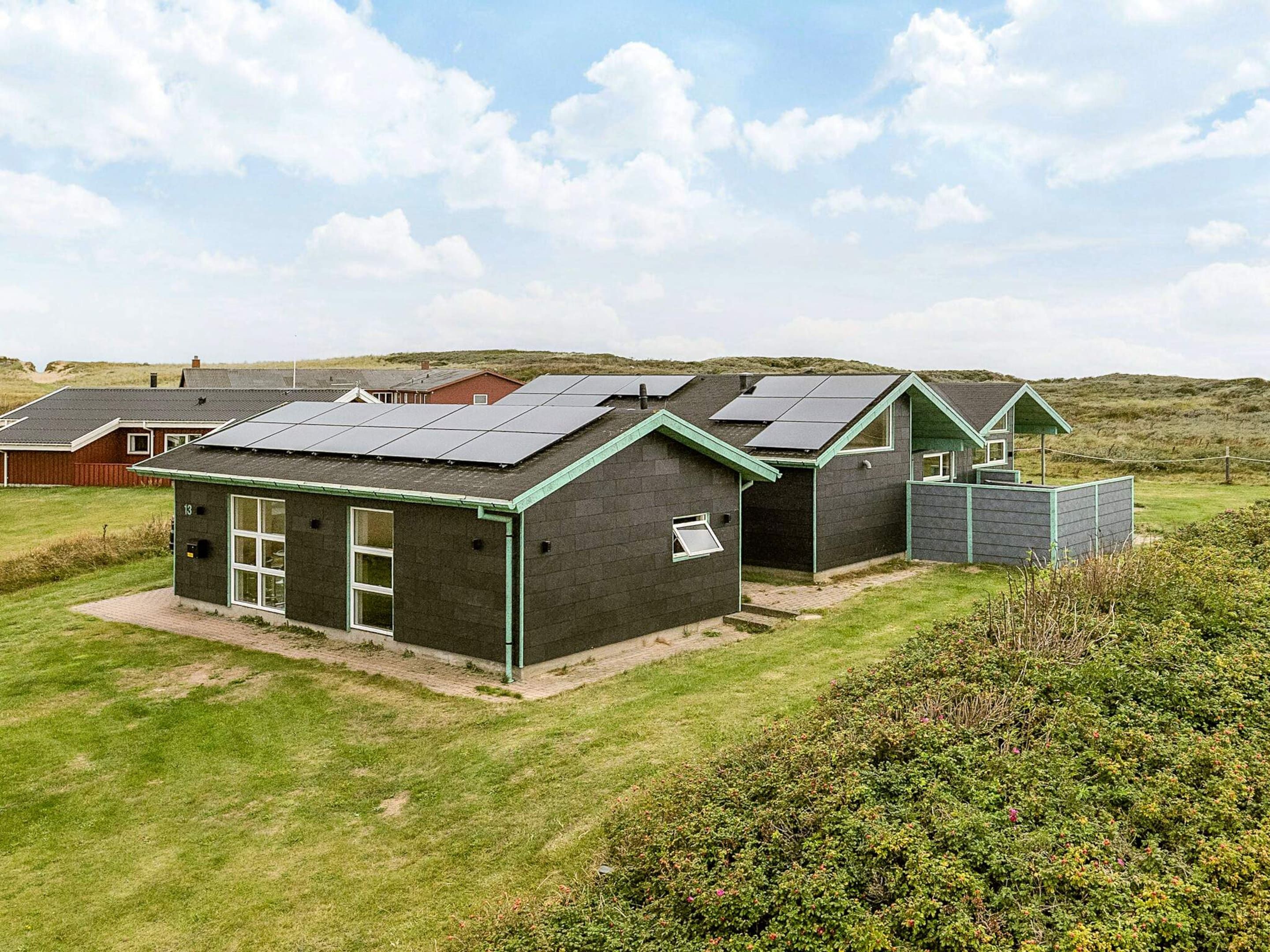 A modern building with solar panels on the roof, surrounded by a grassy area and a hill in the background.