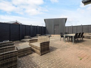 A rooftop patio with wicker furniture and a table, enclosed by a metal fence.