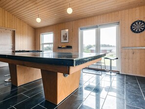 A billiards table in a room with wooden walls and large windows.