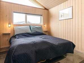 A bedroom with a bed, wooden walls, a window, and a framed picture on the wall.