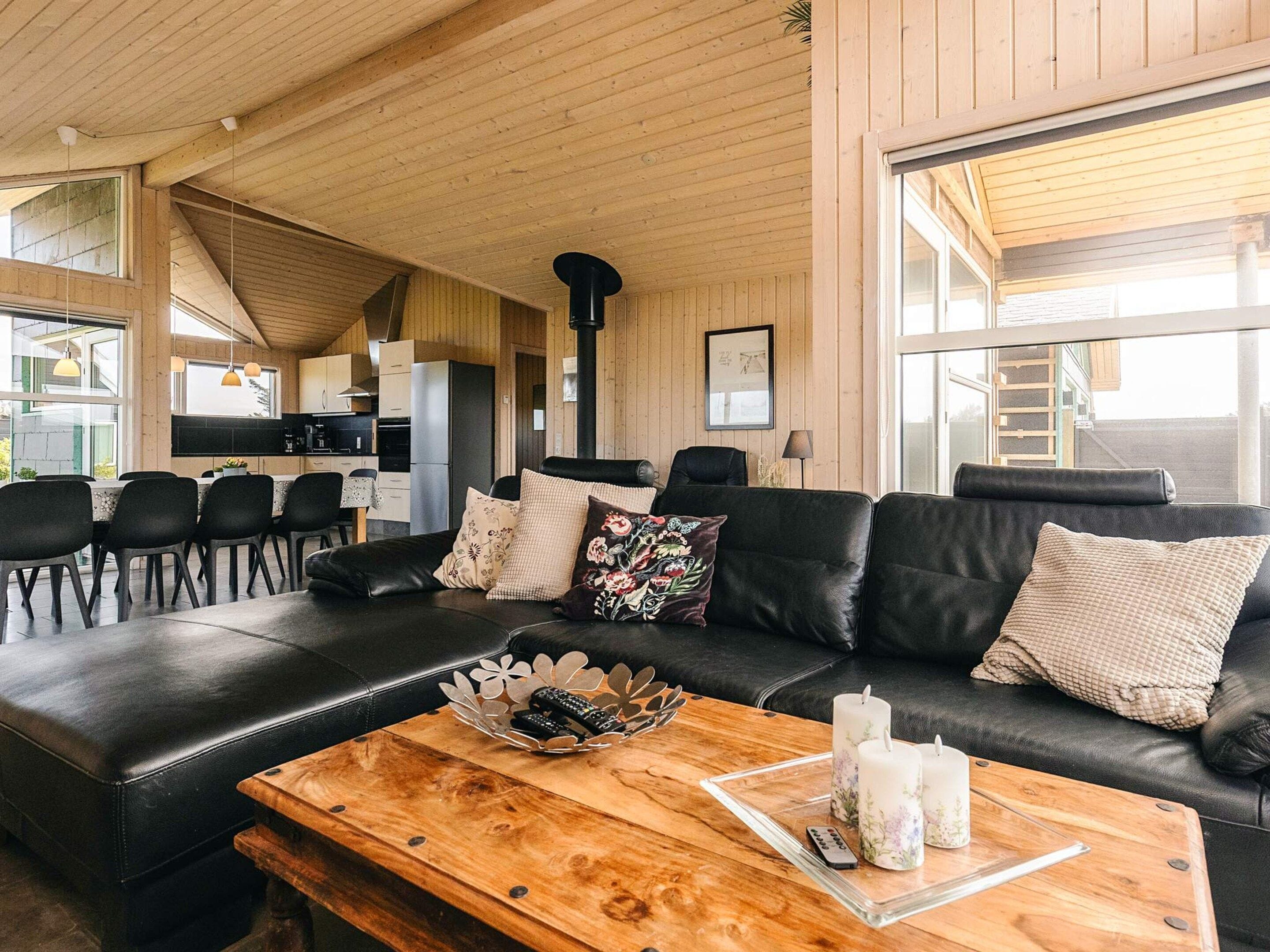 A cozy living room with a black leather sofa, wooden coffee table, and a dining area with chairs and a kitchen in the background.