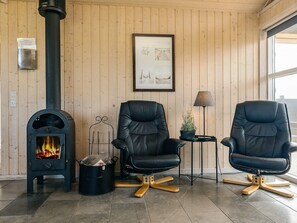 A room with a wood-burning stove, two leather chairs, a small table with a lamp, and a framed picture on the wall.