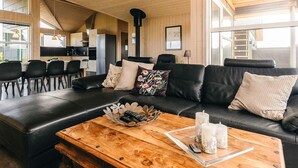 Un salon chaleureux avec un canapé en cuir noir, une table basse en bois et un coin repas donnant sur une cuisine en arrière-plan.