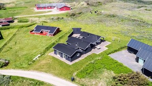 Il s’agit d’une propriété située sur la côte, comprenant plusieurs bâtiments, notamment une maison principale avec un grand garage, un petit bâtiment rouge et une structure noire dotée de panneaux solaires.