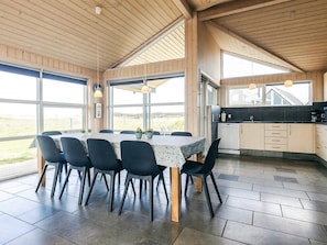 A spacious dining area with a large table and chairs, a kitchen with cabinets and appliances, and large windows offering a view of the outdoors. - 5 Star Holiday Home in Lokken (Lokken)