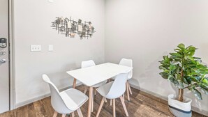 A modern dining area with a white table and chairs, a decorative wall piece, and a potted plant. - Cozy 2BR Suite Close to Downtown w Fast Wifi (Austin)