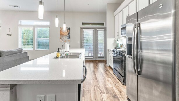 A modern kitchen with a large stainless steel refrigerator, a central island with a sink, and a dining area with a gray sofa. - Cozy 2BR Suite Close to Downtown w Fast Wifi (Austin)