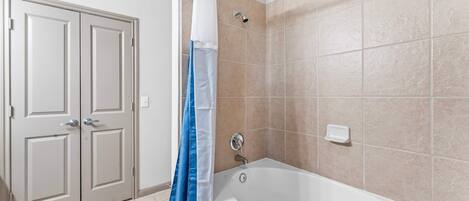 A bathroom with a bathtub, beige tiled walls, a white door, and a blue shower curtain.