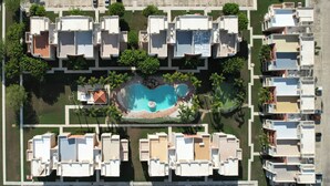 Eine Vogelperspektive eines Wohnkomplexes mit mehreren Wohngebäuden, einem zentralen Schwimmbecken und umgebender Bepflanzung.
