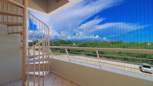 Ein Balkon mit Blick auf eine Straße und Grünflächen, eine Wendeltreppe und ein Fliesenboden.