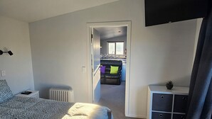 Ein Schlafzimmer mit Bett, Nachttisch, Heizkörper, Kleiderschrank und Blick zur Küche.