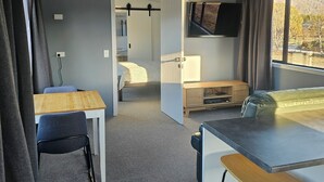 Ein kleines Zimmer mit Bett, Schreibtisch, Stuhl, einem kleinen Tisch und einem an der Wand befestigten Fernseher.