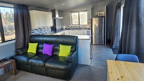 Ein modernes Wohnzimmer mit einem schwarzen Ledersofa, einem Holztisch und Blick zum Küchenbereich.