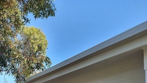 A single-story building with a white exterior, large windows, and a wooden deck. - Family beach house among the gum trees (Ocean Grove)