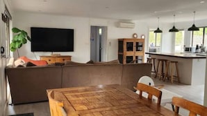 A modern living room with a wooden dining table, a large sectional sofa, and a flat-screen TV. - Family beach house among the gum trees (Ocean Grove)