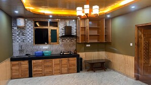 A kitchen with a marble countertop, wooden cabinets, a built-in stove, and a ceiling light fixture. - Redrosecottages  (Manali)