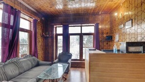 A cozy room with a wooden ceiling, a sofa, a glass-top coffee table, and a wooden counter with a sink. - Redrosecottages  (Manali)
