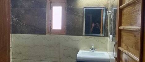A bathroom with a marble wall, a wooden door, a sink, and a mirror.
