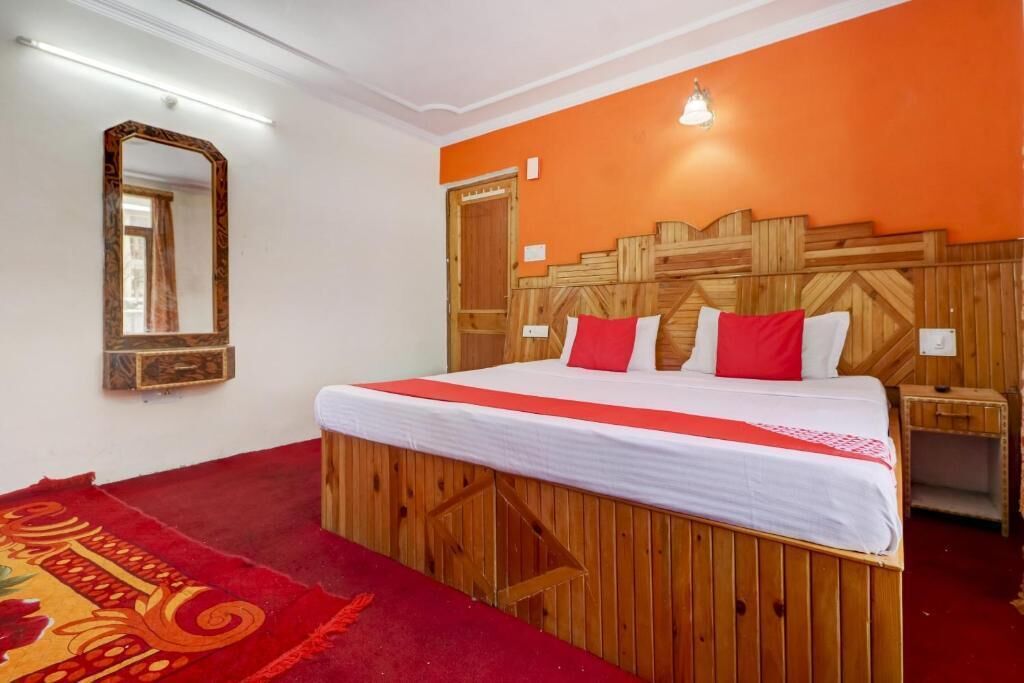 Ein Hotelzimmer mit einem Holzkopfteil, einem großen Spiegel, einer rot-weißen Bettdecke und einem roten Teppich.