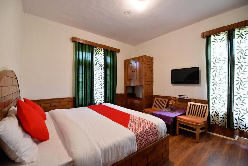A hotel room with a bed, a TV, a wooden cabinet, and a seating area with a chair and table.