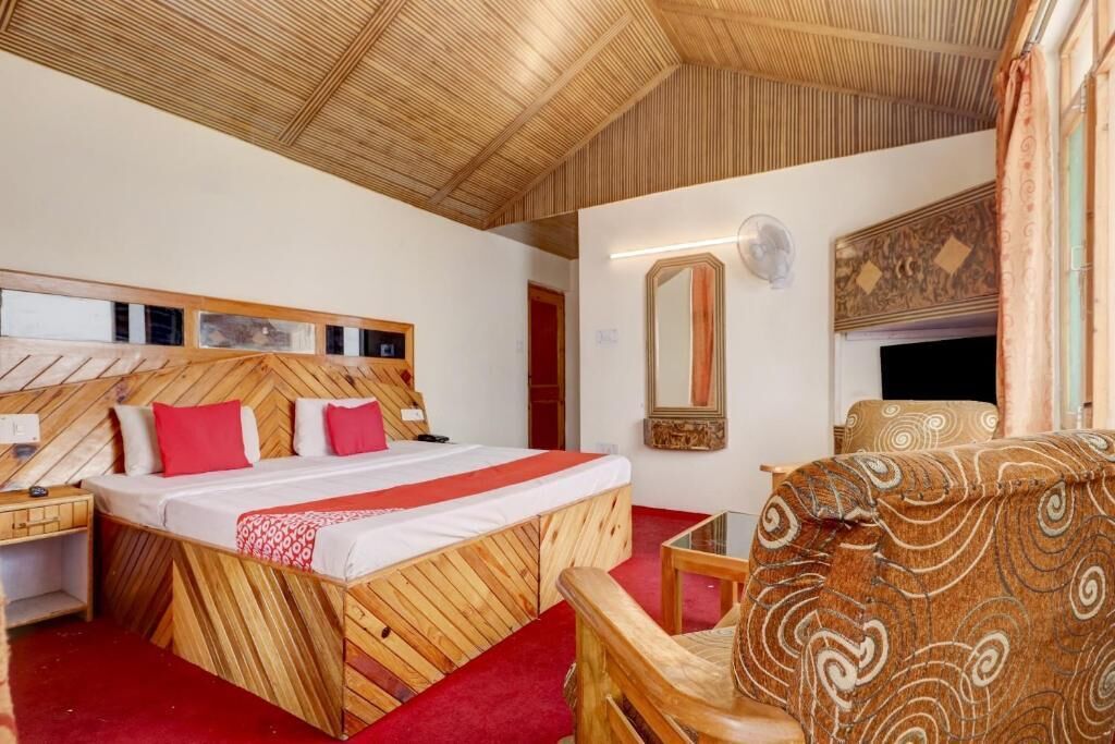 Une chambre avec un lit doté d’une tête de lit en bois, une moquette rouge, une chaise en bois et un grand miroir au mur.