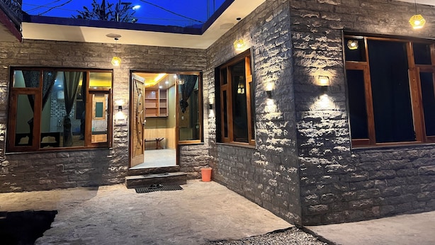 A modern house with stone exterior walls, large windows, and a well-lit entrance. - Redrosecottages  (Manali)