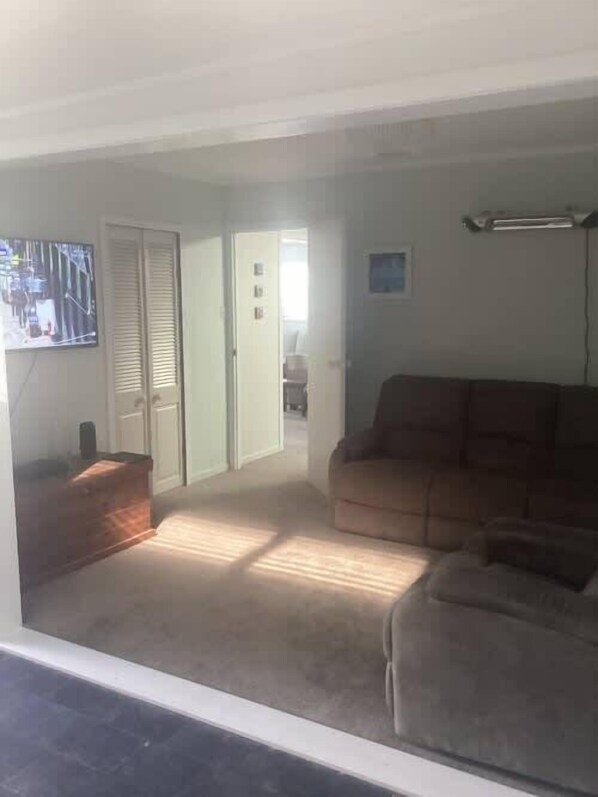 A living room with a couch, a television, and a door leading to another room. - Hosts on Coast Casement Fun (Whangamata)
