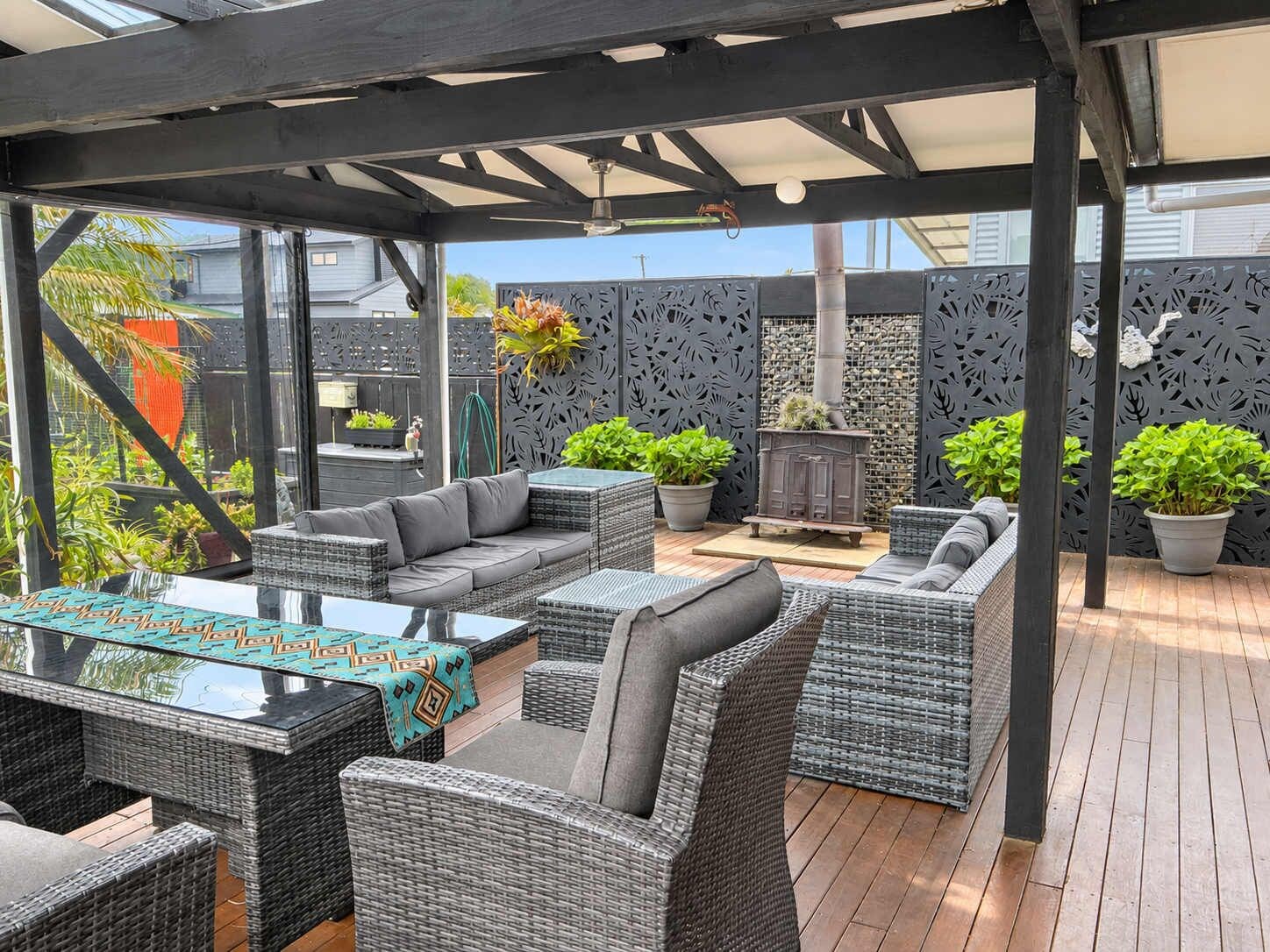 Une terrasse extérieure avec des meubles en osier, une table à plateau en verre et des plantes en pot.