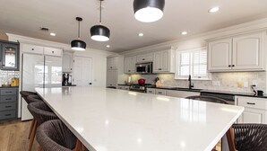 A modern kitchen with white cabinetry, a large island, and black pendant lights.