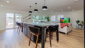 A modern kitchen with a central island, bar stools, pendant lighting, and a large window providing natural light.