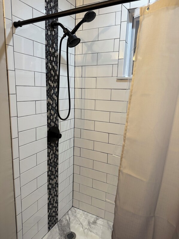 A shower with a black and white tiled wall, a showerhead, and a curtain.