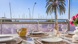 Una mesa lista para comer con vistas al mar y a los barcos, una botella de vino y un jarrón con flores.