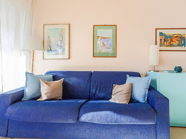 En blå sofa med puder, en lampe og indrammede kunstværker på væggen.