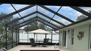 A covered outdoor swimming pool with a table and chairs, a pool ladder, and a view of the backyard.
