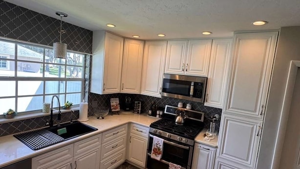 A kitchen with white cabinets, a stainless steel stove, a microwave, and a sink.