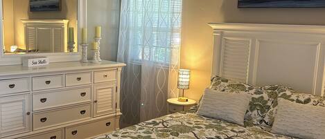 A bedroom with a bed, dresser, ceiling fan, and a window with curtains.